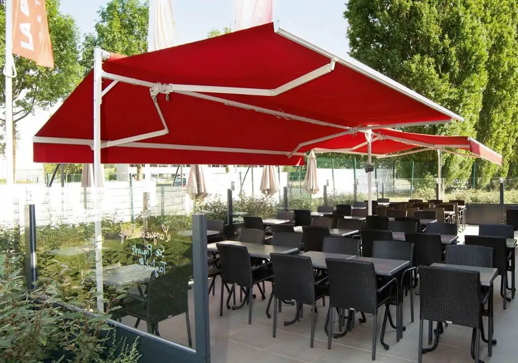 Deux abris de terrasse à double pente et toile rouge au-dessus des tables d’une terrasse de restaurant