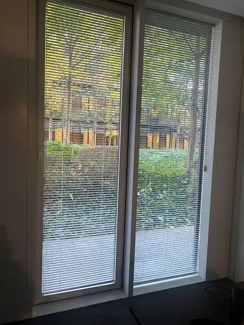 Store vénitien blanc baissé devant une porte-fenêtre qui donne sur un jardin, au siège d’APICIL