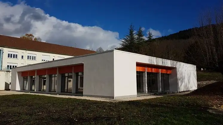 Le bâtiment et ses stores orange, au pied de l’hôpital et des collines boisées