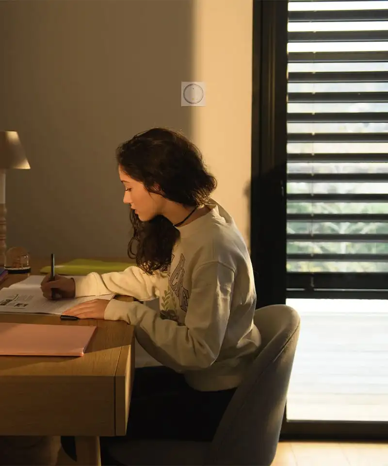 Jeune femme travaillant à son bureau, lumière du jour filtrée par les lames d’un brise-soleil orientable