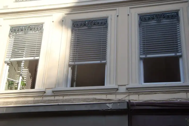 Façade d’immeuble lyonnais : brise-soleil orientables gris clair derrière les cantonnières en fonte des fenêtres