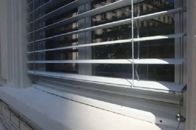 Brise-soleil baissé devant une fenêtre d’immeuble ancien, son câble de guidage tendu jusqu’à l’appui