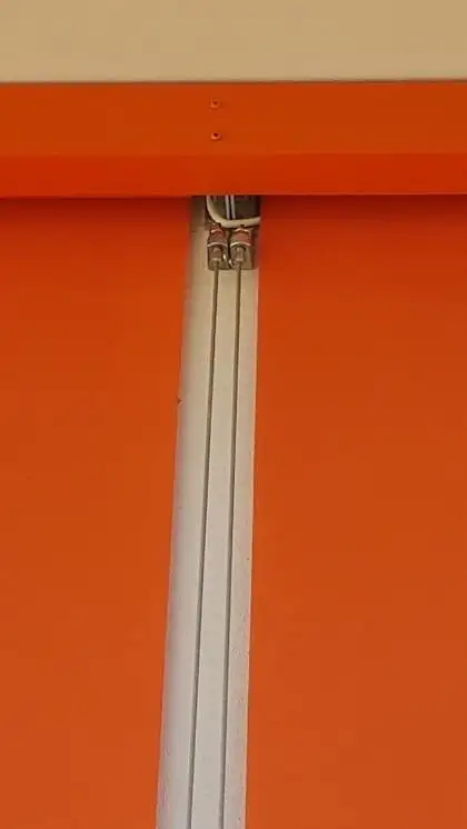 Détail d’un store orange : le haut de la toile et son guidage latéral