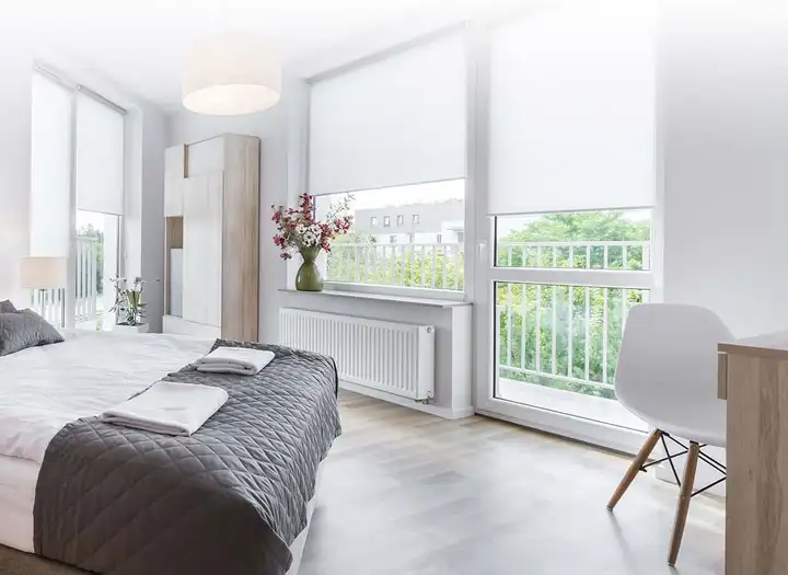 Chambre claire : stores enrouleurs blancs à mi-hauteur devant les portes-fenêtres, le jardin visible dessous