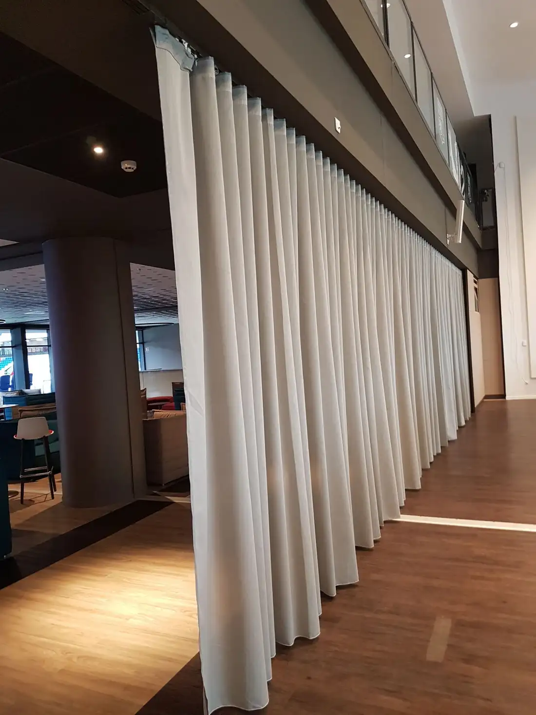 Rideau blanc à plis réguliers tombant du plafond jusqu’au parquet, au salon du Groupama Stadium