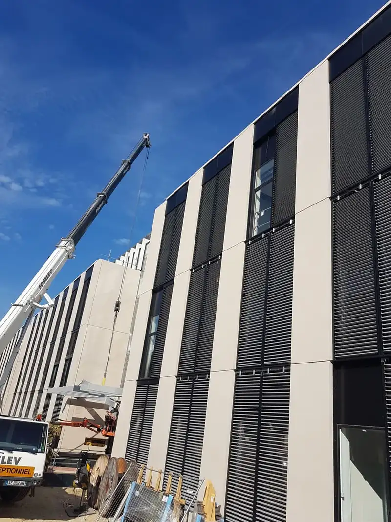 Chantier du pavillon H : brise-soleil posés sur la façade, grue au pied du bâtiment
