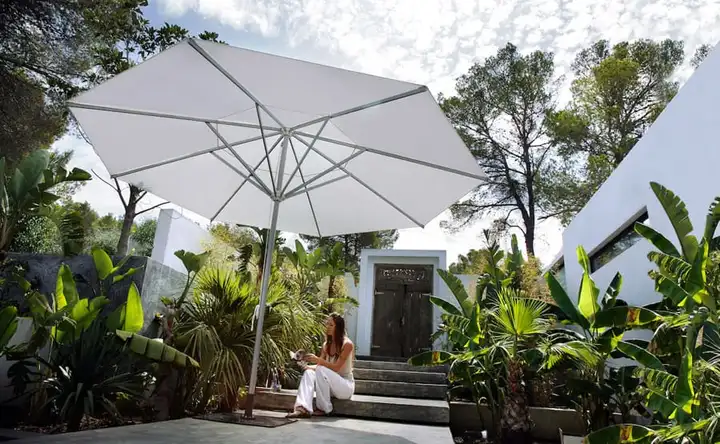 Grand parasol droit à toile blanche au milieu d’un jardin tropical, devant une maison contemporaine