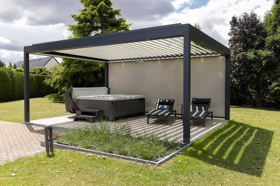Pergola à lames autoportée sur une pelouse, un spa et deux transats à l’abri