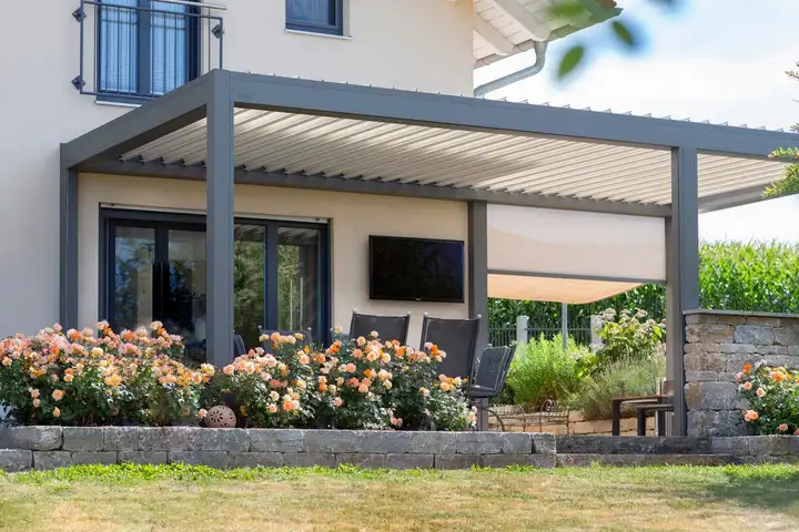 Pergola grise à lames adossée à une maison, un screen déroulé sur le côté de la terrasse