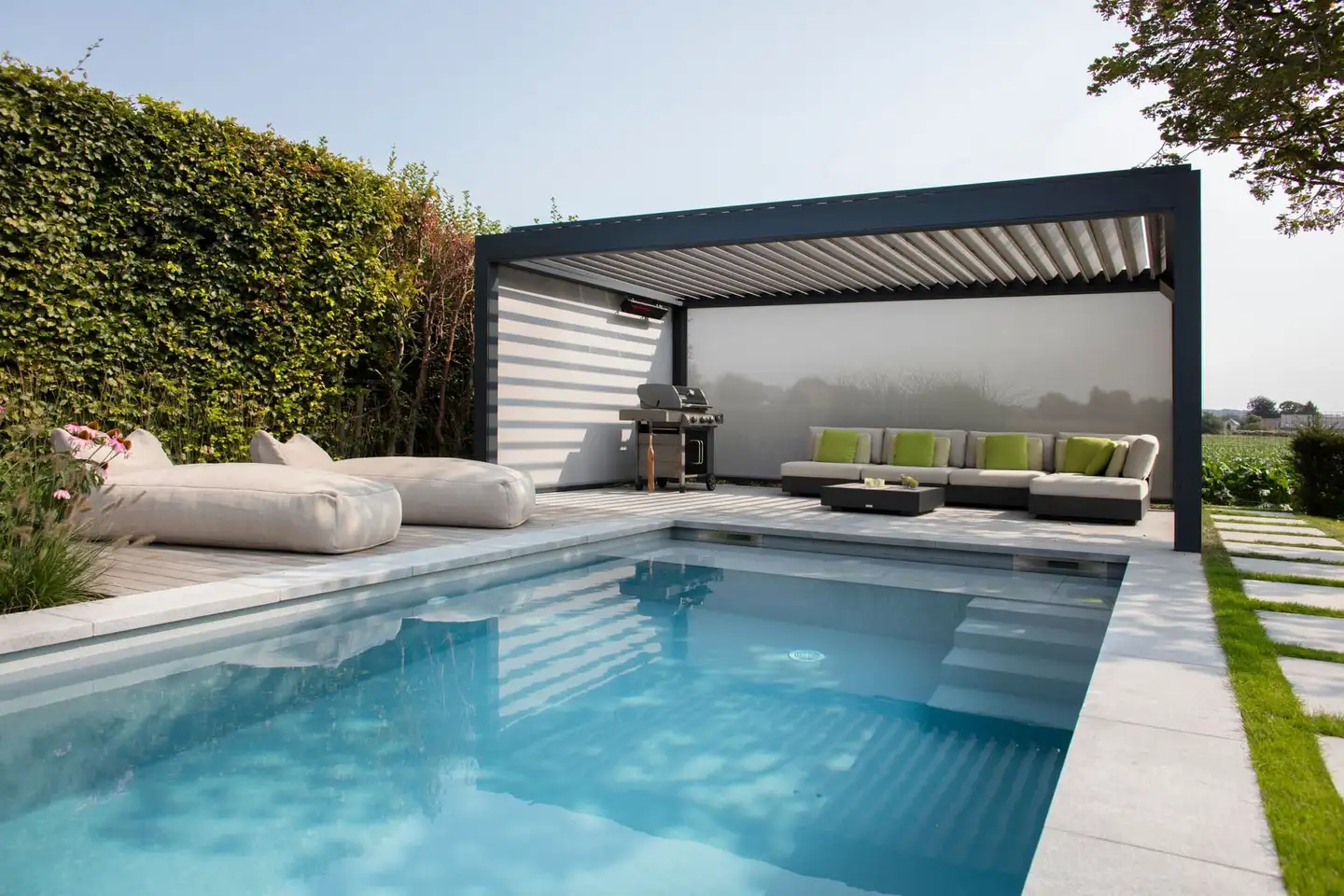 Pergola bioclimatique anthracite à lames orientables au bord d’une piscine, salon d’extérieur à l’ombre