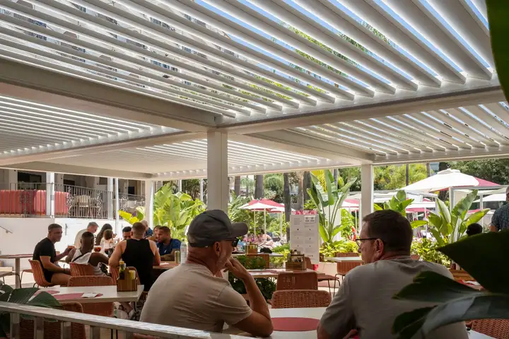 Terrasse de restaurant animée sous une grande pergola blanche à lames orientables