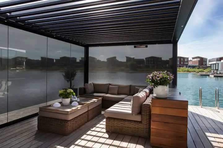 Pergola à lames fermée par des parois de verre, un salon d’extérieur face à un lac