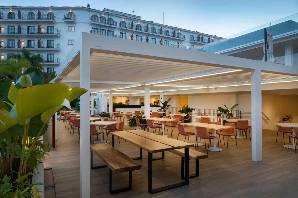 Terrasse de restaurant d’hôtel couverte d’une grande pergola bioclimatique blanche, éclairée par des LED intégrées