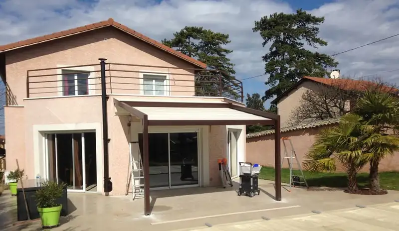 Pergola à toile claire sur poteaux bruns, au-dessus de la terrasse d’une maison