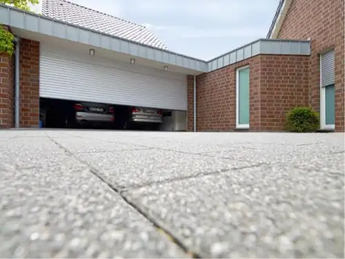Porte de garage enroulable blanche à demi ouverte sur un double garage, dans une maison en brique