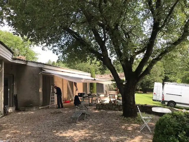 Le store en cours de rentoilage, vu depuis le jardin, sous un grand arbre