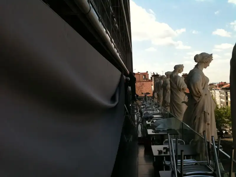La toile du store de la terrasse, tendue le long de la façade, face aux statues