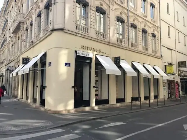 Angle d’un immeuble lyonnais dont les vitrines Rituals sont abritées par des bannettes blanches