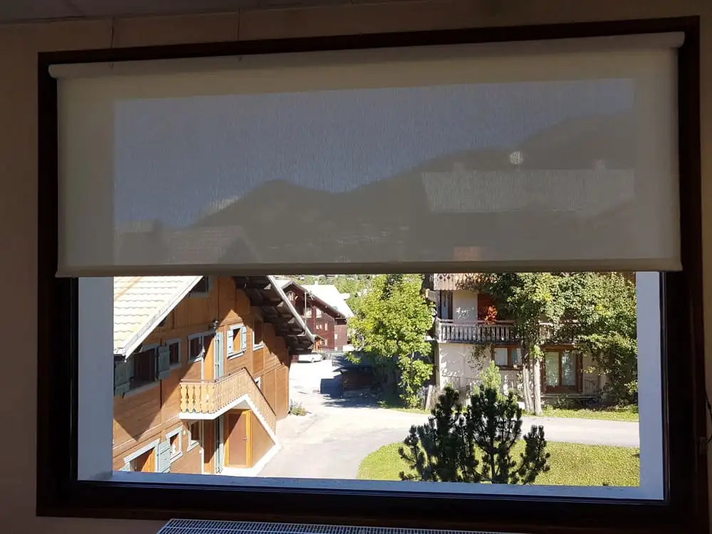 Store enrouleur à toile screen baissé à mi-hauteur devant une fenêtre ouverte sur les chalets de Châtel