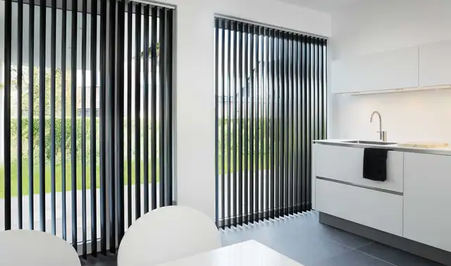 Stores à bandes verticales noires devant les baies vitrées d’une cuisine blanche