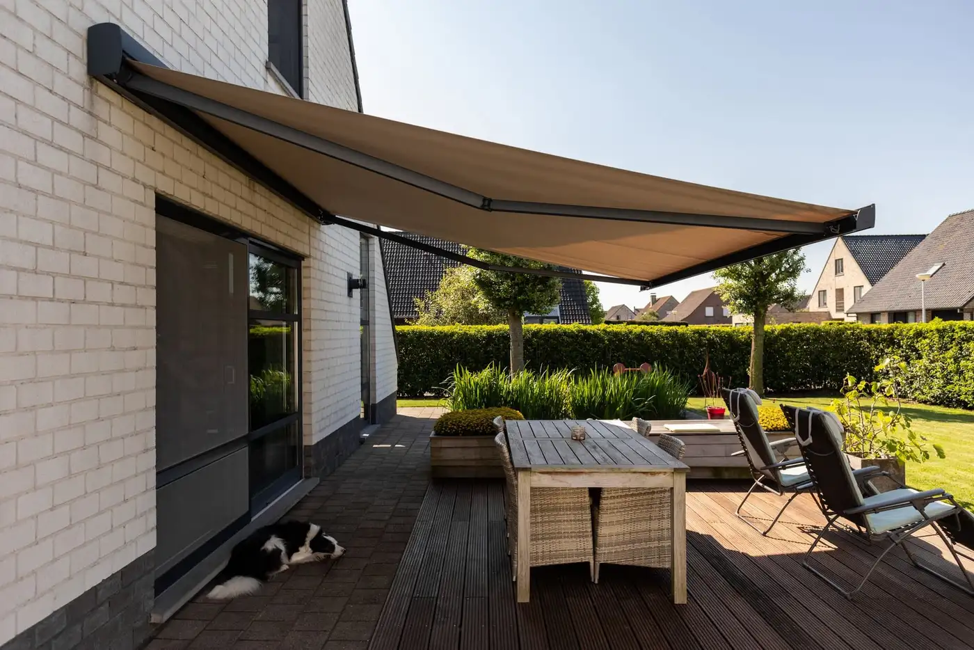 Store banne à coffre, toile taupe, déployé au-dessus de la terrasse en bois d’une maison
