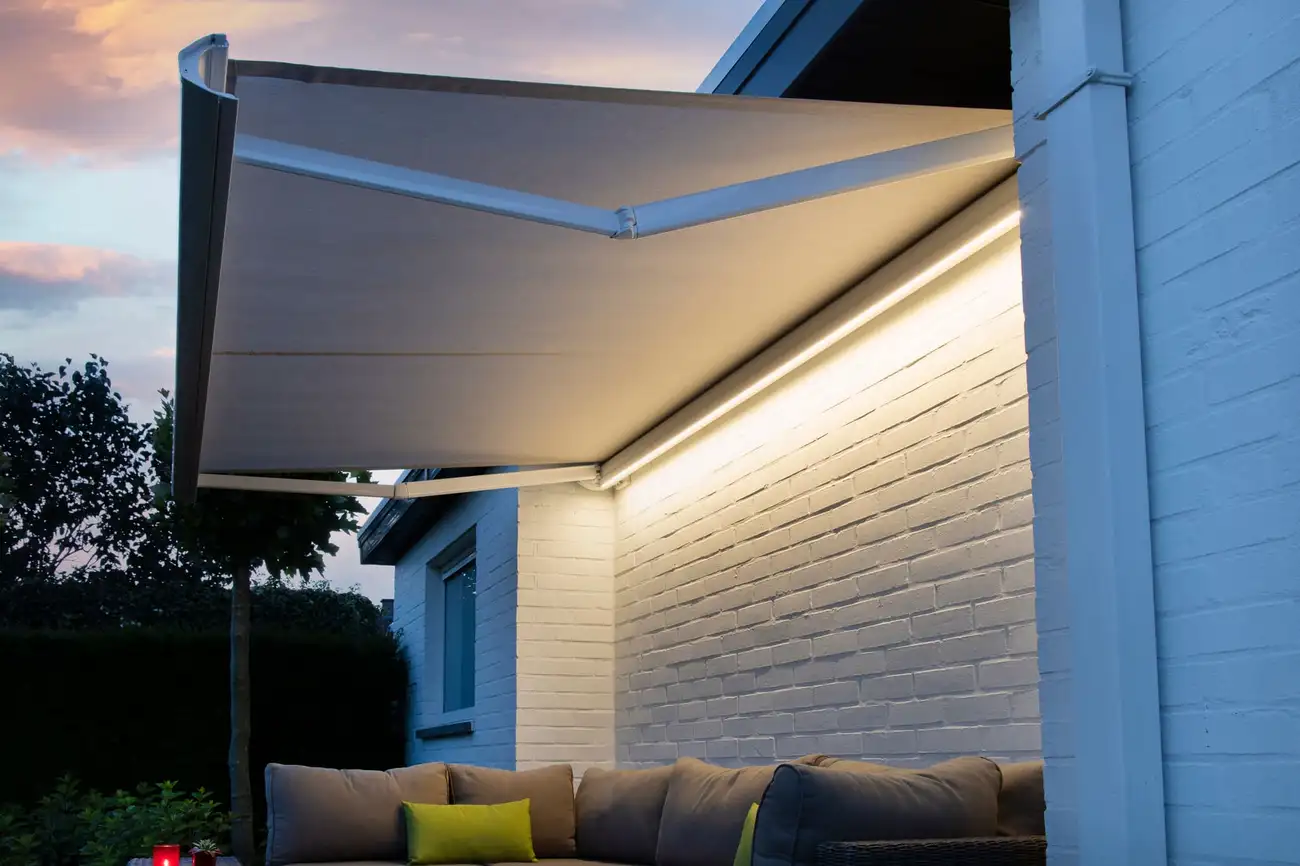 Store banne éclairé au crépuscule par une rampe lumineuse le long du mur, au-dessus d’un canapé de jardin