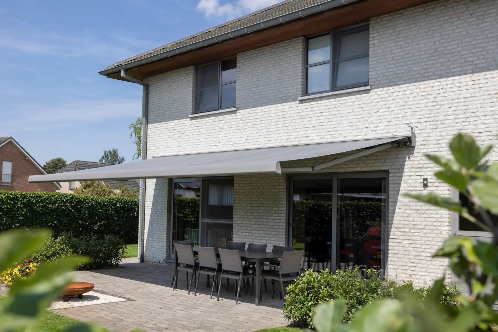 Store banne à coffre et toile grise déployé sur toute la largeur d’une maison, au-dessus de la terrasse