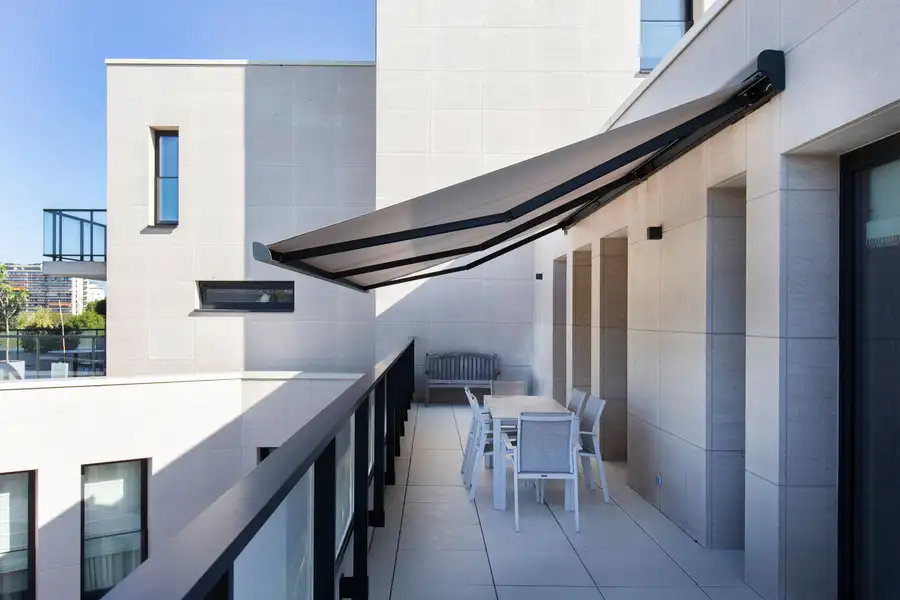 Store banne gris déployé au-dessus de la terrasse d’un appartement en étage, table et chaises dessous