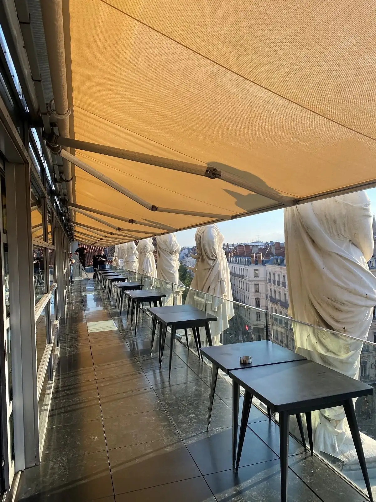 Terrasse de l’Opéra de Lyon sous son store banne, entre les statues du toit