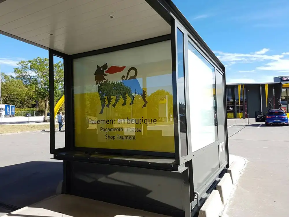 Guichet vitré d’une station-service, habillé d’un store enrouleur imprimé aux couleurs de l’enseigne