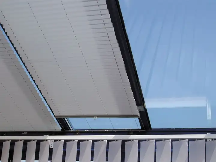 Store plissé blanc tendu sous une fenêtre de toit inclinée, le ciel bleu derrière