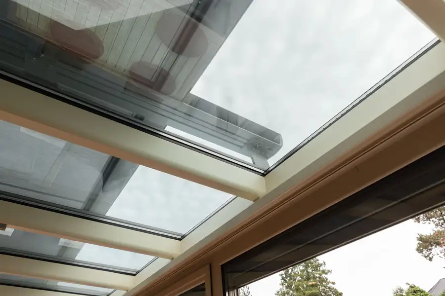 Vue depuis l’intérieur d’une véranda : la toile d’un store extérieur tendue au-dessus de la toiture vitrée