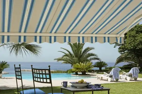 Toile de store banne rayée bleu et écru, déployée au-dessus d’une terrasse face à la mer