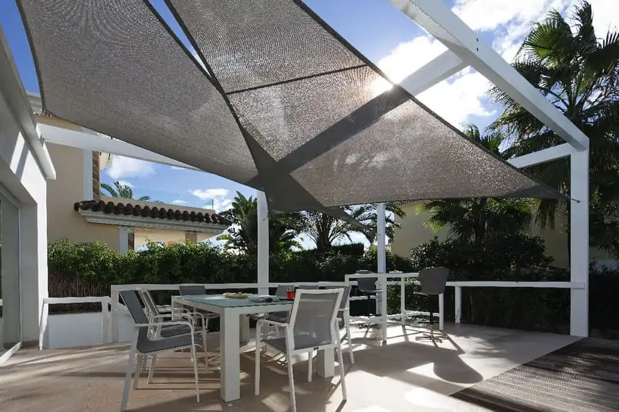 Voiles d’ombrage grises tendues au-dessus d’une table de jardin, sur une terrasse blanche