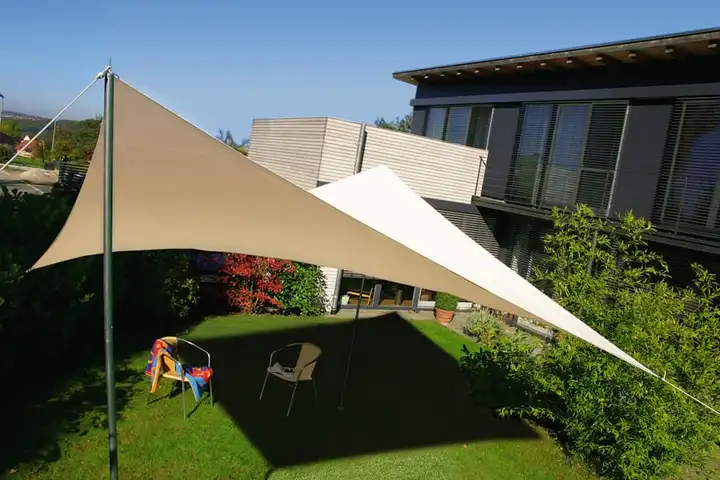 Voiles d’ombrage triangulaires claires tendues au-dessus d’une pelouse, devant une maison