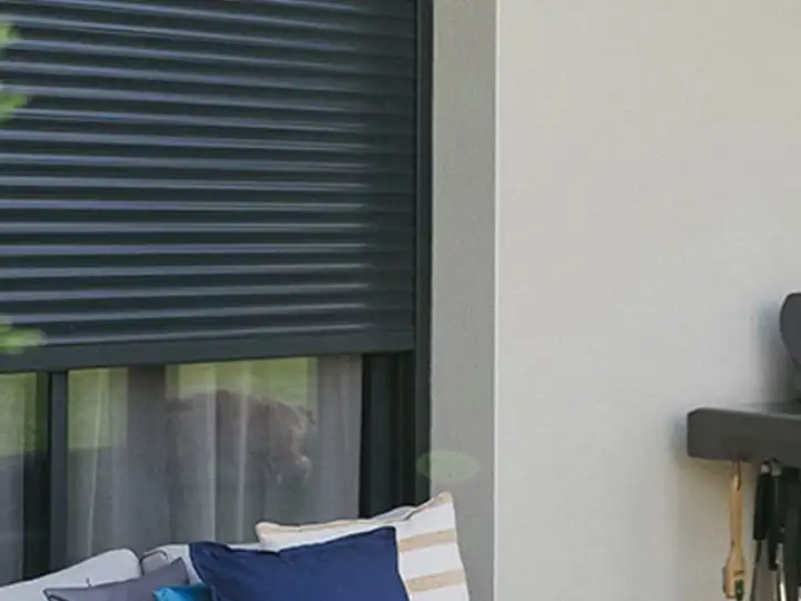 Volet roulant gris anthracite à demi baissé devant une baie, sur une façade claire